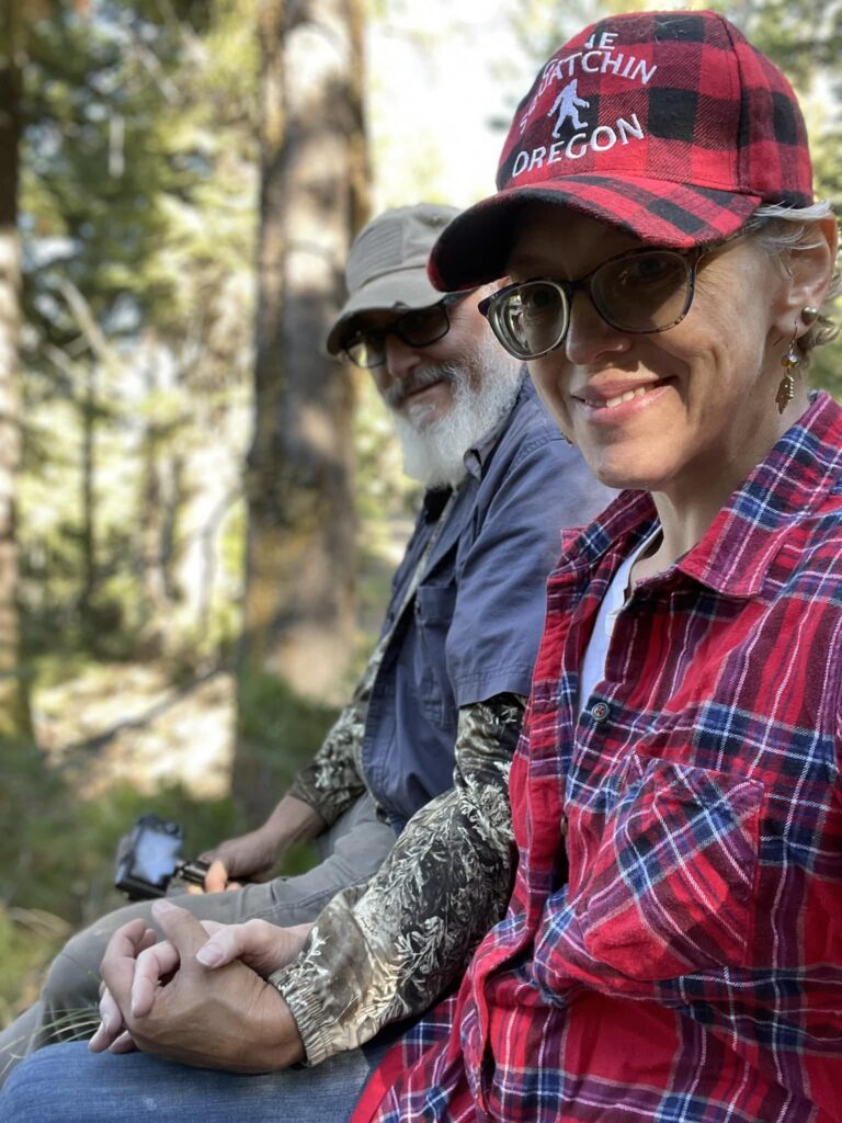Reconnection and peace: Together, we found our wild truth amidst the trees. Two people sitting in the woods holding hands, surrounded by sunlight and trees, symbolizing reconnection, peace, and the joy of being present together in nature.